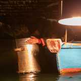 ...e, sporgendosi leggermente dalla barca, regge con entrambe le mani il contenitore cilindrico in metallo. Il fondo in vetro � immerso in acqua e gli serve per scorgere eventuali banchi di pesci